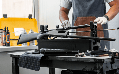 Person assembling rifle on workshop table.