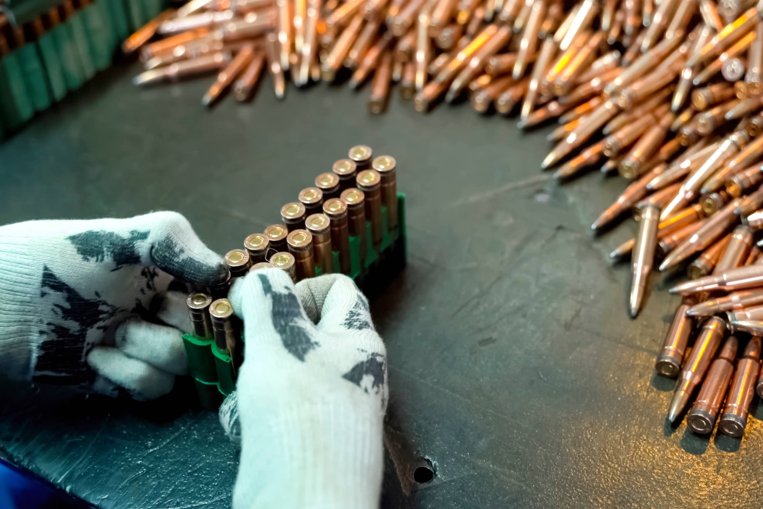 Gloved hands arranging bullets on table.